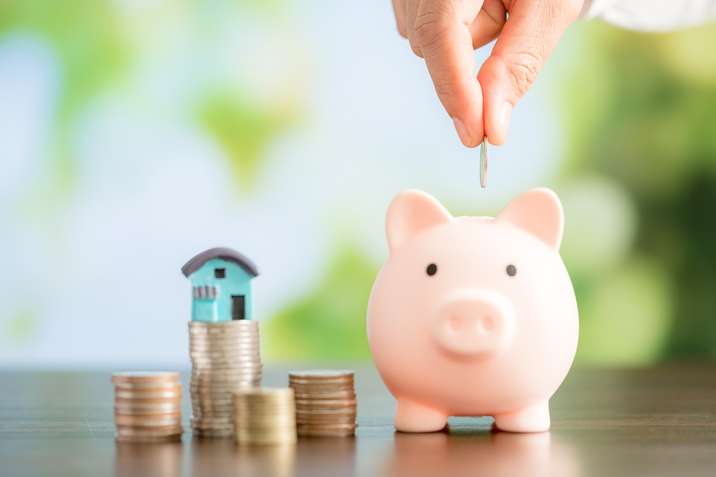 Hand putting coin in a piggy bank. Saving money concept to buy a house.